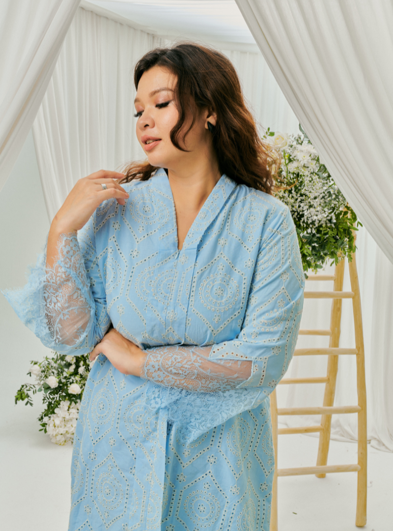 A woman dressed in Baby Blue Tun Farah Embroidered Eyelet Kurung