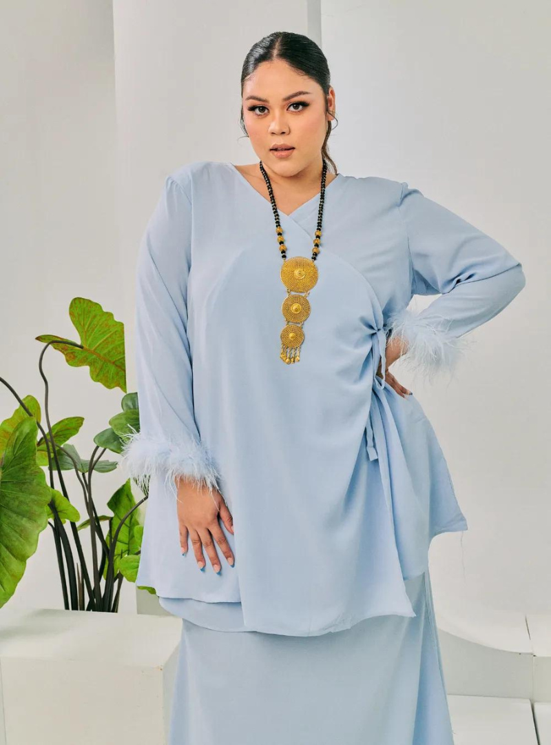 A woman dressed in Baby Blue Tun Malika Feather Wrap Kurung